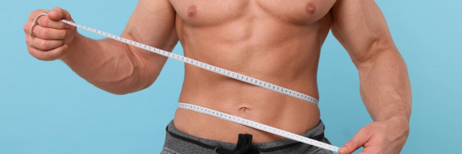 Man checks his waist with a tape measure against a blue background, emphasizing fitness on the go for travelers.