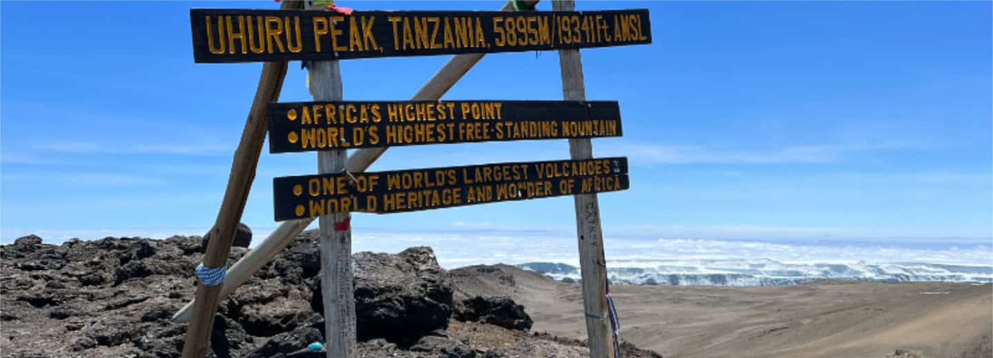 Wooden signs at Uhuru Peak, Mount Kilimanjaro, mark the summit—a challenging hike perfect for travelers staying fit on the go.