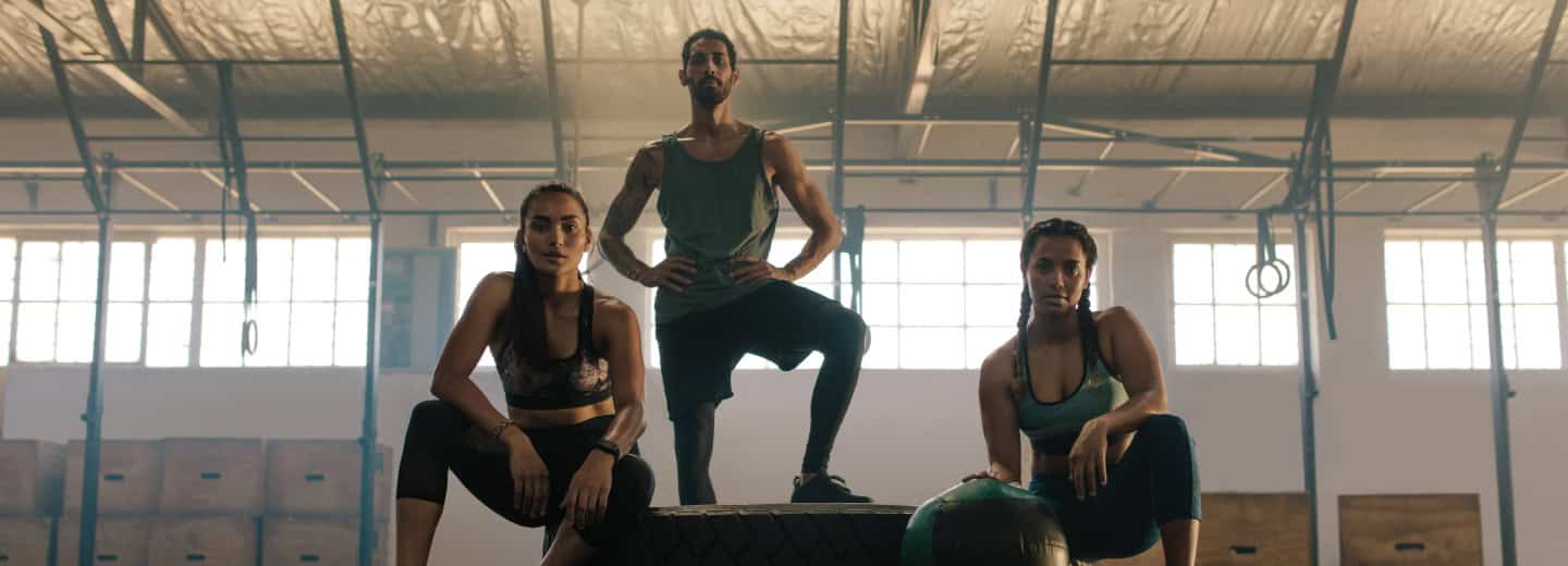 Three travelers in athletic wear pose confidently in a hotel gym, showing how it's possible to stay fit while on the road.
