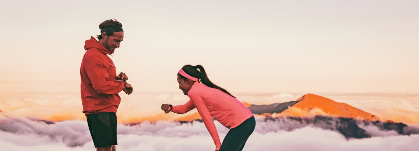 Two travelers in sportswear check watches and smile after a sunrise run, showing it's easy to stay fit on the go with HotelGyms.com.
