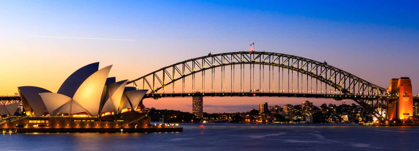 Sydney Opera House and Harbour Bridge at sunset, city lights reflecting on water—a scenic spot for travelers to stay active outdoors.