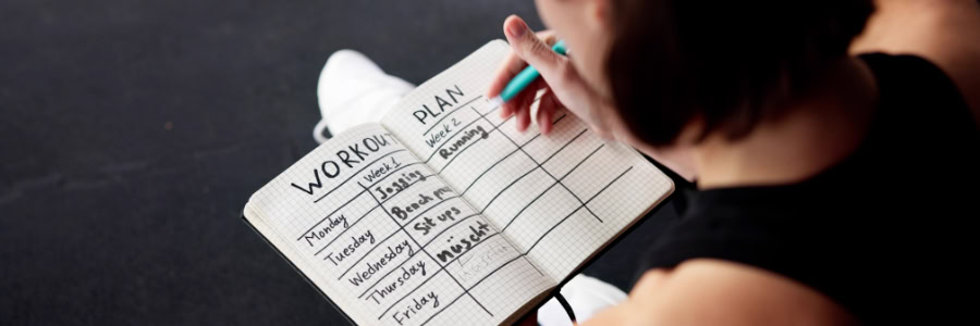 Traveler creating a weekly fitness plan in a notebook, outlining daily workouts to stay active while away from home.