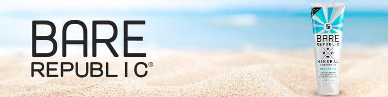 Bare Republic mineral sunscreen tube sits on sandy beach, ocean and sky behind—perfect for sun protection during active travel.