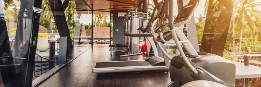 Stay fit while traveling in this modern hotel gym featuring treadmills, exercise machines, and large windows with tropical views.